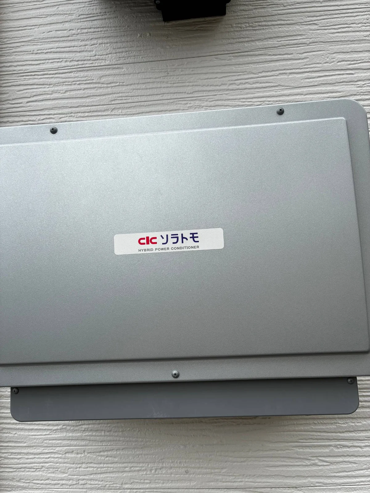 長州産業のハイブリッドパワコン PCS-55RH2A。屋外の外壁に付いた銀色の箱で「ソラトモ HYBRID POWER CONDITIONER」のシール